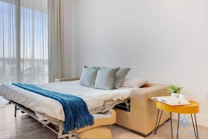 A modern bedroom with a bed, a small side table, and a view through large windows.