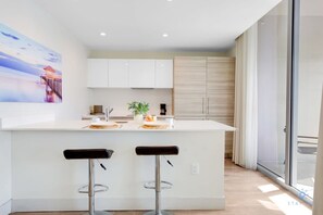 A modern kitchen with a central island, two bar stools, and a large window providing natural light. - Brand New Apt | Rooftop Pool | Beach Access (Hollywood)