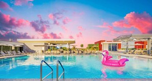 A swimming pool with a pink flamingo float, lounge chairs, and a modern building with a flat roof. - Brand New Apt | Rooftop Pool | Beach Access (Hollywood)