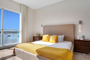 A hotel room with a large window, a bed with yellow bedding, a nightstand, and a wall-mounted light fixture. - Brand New Apt | Rooftop Pool | Beach Access (Hollywood)