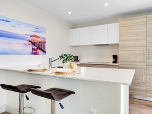 A modern kitchen with white cabinetry, a central island with stools, and a large window with a view of a pier.