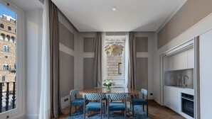 A dining area with a wooden table and blue upholstered chairs, a blue rug, and a view of a historic building through a window. - Palazzo Signoria Luxury Apartments (Florence)