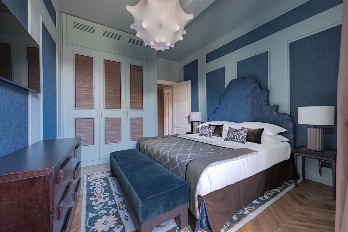 A bedroom with a large bed, a wooden dresser, a bench, and a patterned rug.