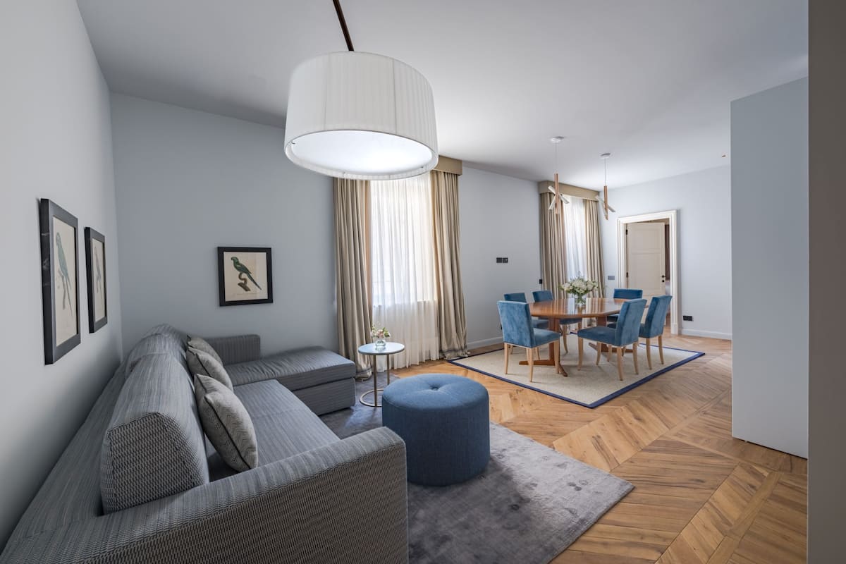 A modern living room with a sofa, ottoman, dining area, and a large pendant light.