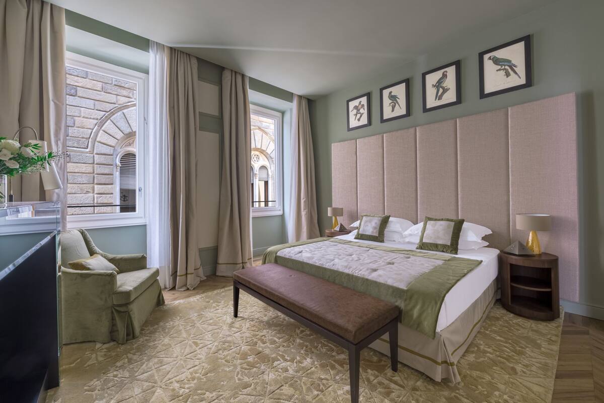 A hotel room with a large bed, a bench, a chair, a desk, and a window with curtains.