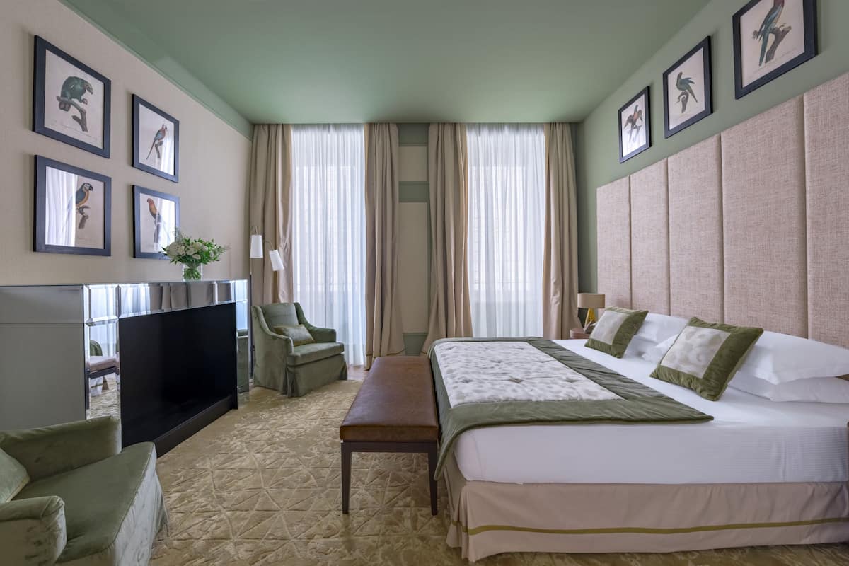 A hotel room with a large bed, a flat-screen TV, a sofa, a bench, and framed artwork on the walls.