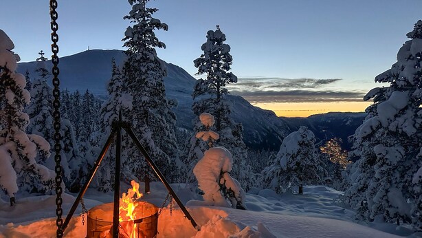 Een sneeuwlandschap met een kampvuur en een berg op de achtergrond.