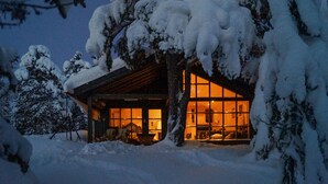 Een knus blokhut met een grote glazen deur, omgeven door met sneeuw bedekte bomen.
