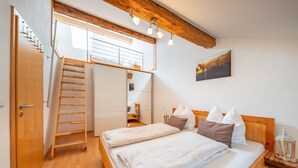 A bedroom with a wooden bed, a ladder leading to a loft, and a painting on the wall. - Ferienwohnung Da Dachstui 60 Qm,1 Schlafzimmer, Wohnschlafraum, bis 6 Personen (Samerberg)