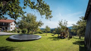 A grassy outdoor area with a trampoline, trees, and a small wooden structure. - Ferienwohnung Da Dachstui 60 Qm,1 Schlafzimmer, Wohnschlafraum, bis 6 Personen (Samerberg)