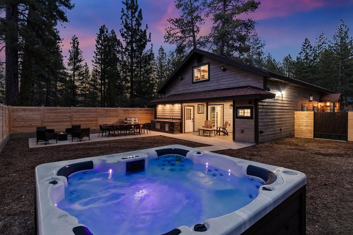 A wooden house with a hot tub in the backyard, surrounded by trees.