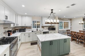 A modern kitchen with white cabinetry, a central island, and a dining area with wooden chairs.