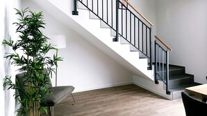 A modern staircase with black railings and wooden handrails, leading to a landing with a dining area. - Schicke Apartments in Osnabrück (Osnabrueck)
