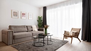 A modern living room with a sofa, a round coffee table, a chair, and framed artwork on the wall. - Schicke Apartments in Osnabrück (Osnabrueck)