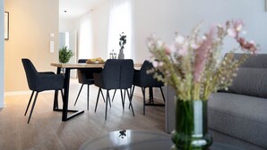 A modern dining area with a wooden table, four chairs, and a vase of flowers. - Schicke Apartments in Osnabrück (Osnabrueck)