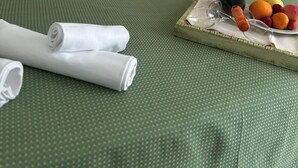 Een net opgemaakt bed met witte lakens, een grof gebreid, groen dekbed en een dienblad met fruit en een fles op de nachtkastje.