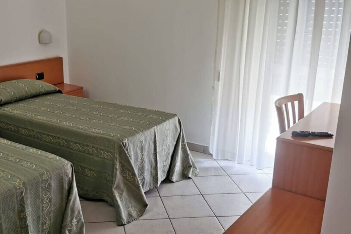 Habitación de hotel con dos camas individuales, cabecera de madera, una mesita con un control remoto y una silla.