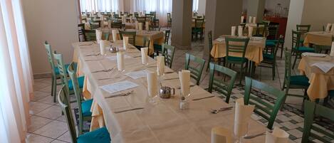 Un comedor con varias mesas dispuestas para el servicio, cada una con sillas verdes y manteles color beige.