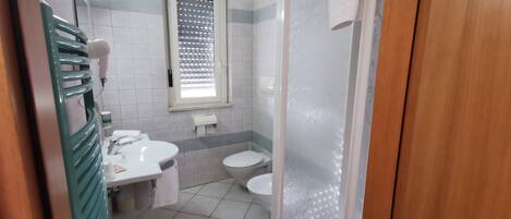 A bathroom with a toilet, sink, and a hairdryer on a stand.