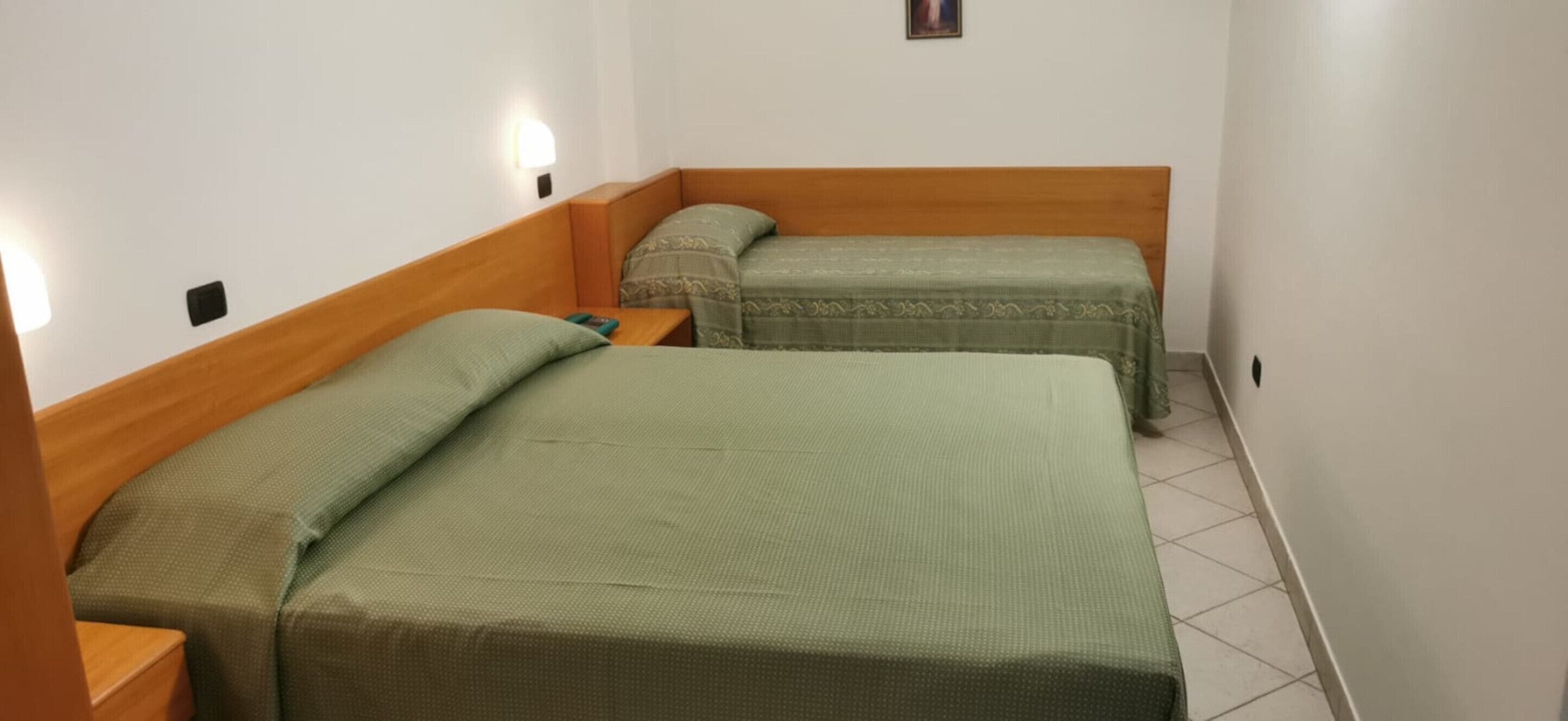 A small, clean room with two single beds, each with a wooden headboard and a green bedspread.
