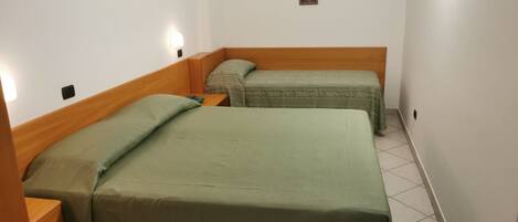 A small, clean room with two single beds, each with a wooden headboard and a green bedspread.