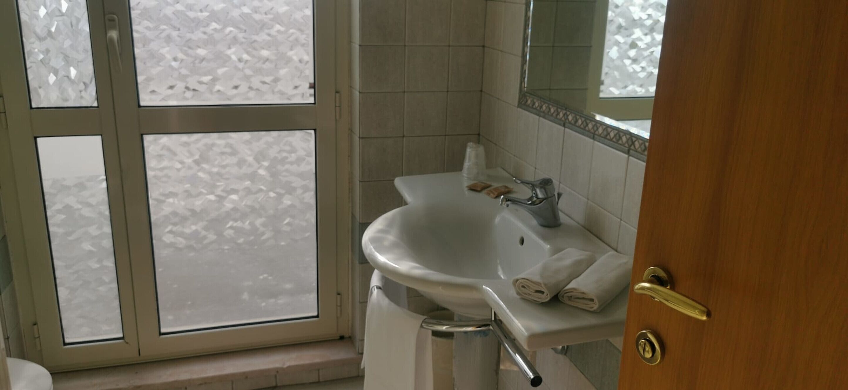 A bathroom with a white sink, a mirror, and a window with frosted glass.