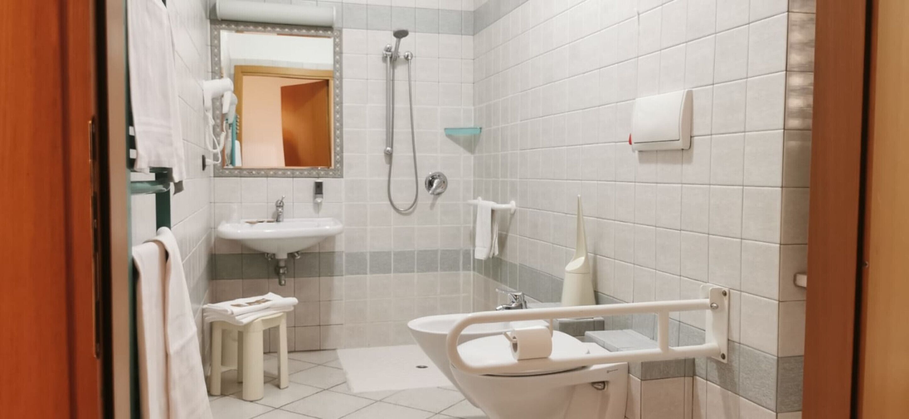 Un baño con lavamanos, espejo, ducha y un inodoro accesible para sillas de ruedas.