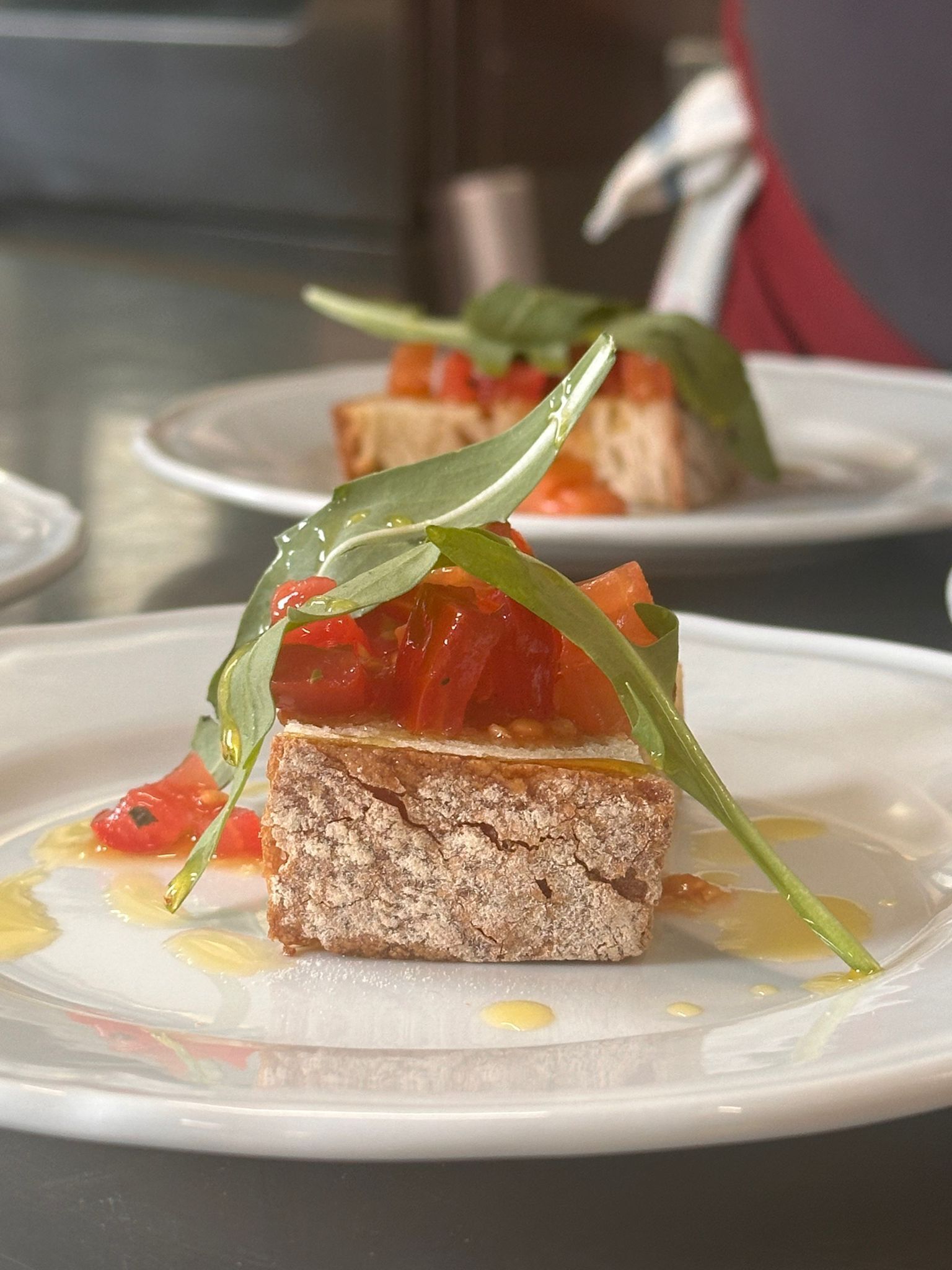A dessert with a slice of bread topped with tomato and green leaves on a white plate.