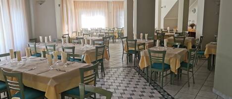 A restaurant with multiple tables and chairs, arranged in a spacious layout with a tiled floor.