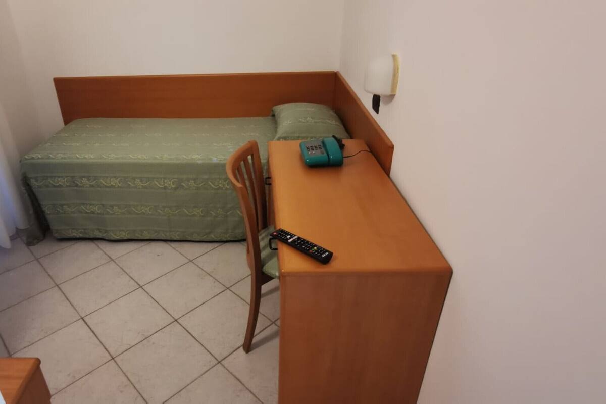 Una habitación pequeña y ordenada con cama, una silla, una mesa y un escritorio.