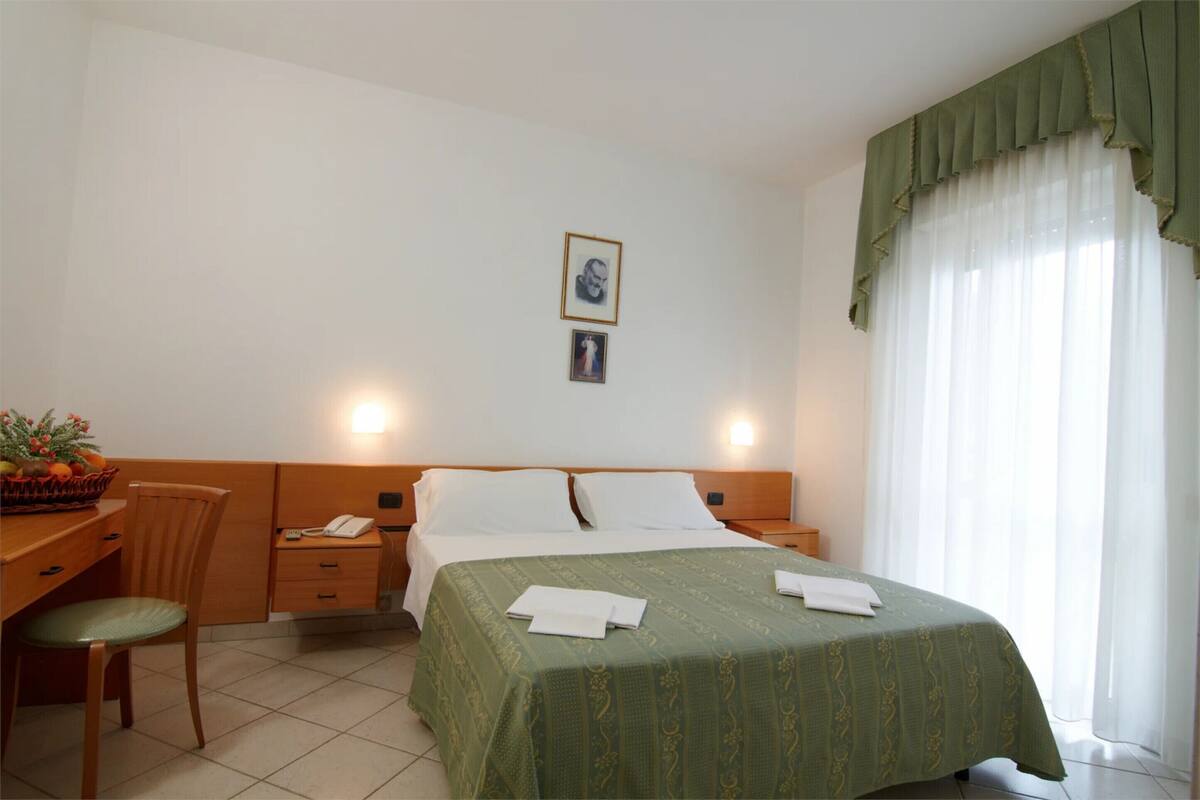 Habitación de hotel con cama, escritorio, silla, mesita de noche y lámpara de pared.