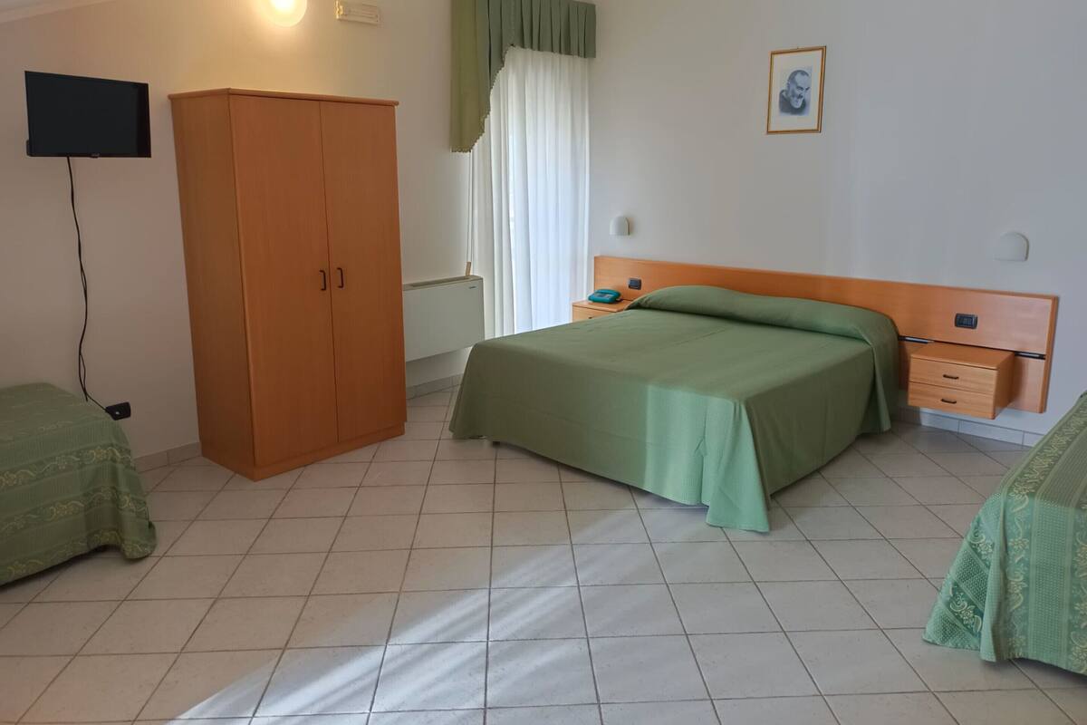 Un dormitorio con cama, armario, mesita de noche, televisor y ventana con cortinas.