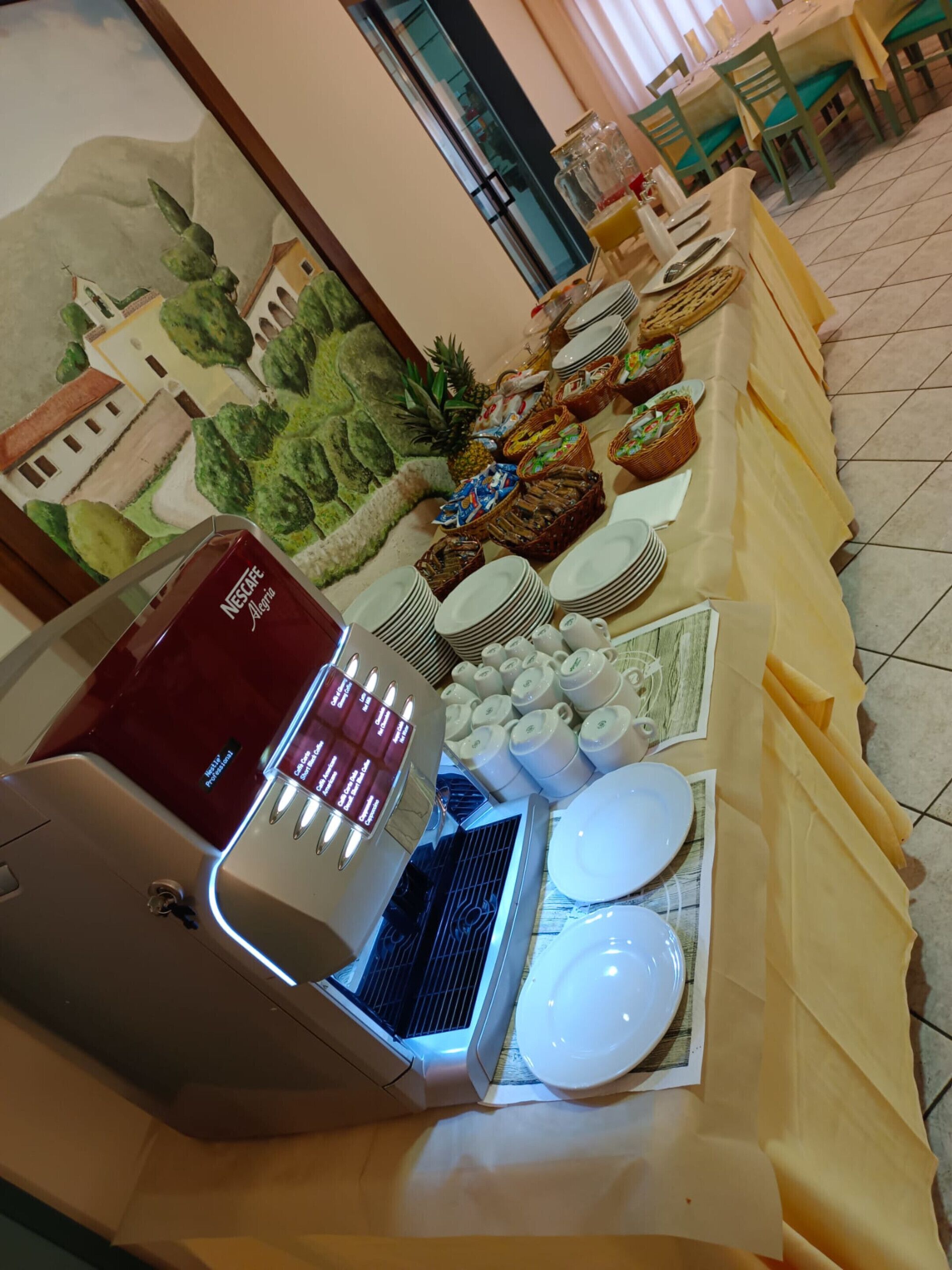 Disposição de buffet com máquina de café, pratos e diversos alimentos.