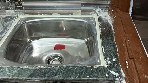 Een keuken met een spoelbak, een kraan en een betegelde achterwand met afbeeldingen van koffiekopjes en koffiebonen.