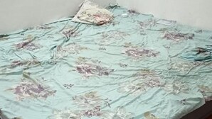 Een bed met een bloemenbedekking in een kamer met een effen muur en een rode vloer.