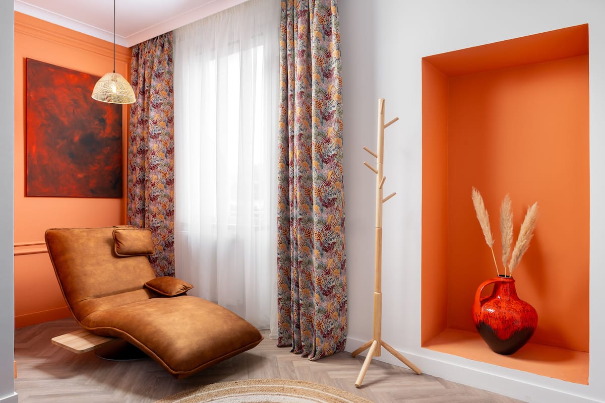 A modern living room with a leather armchair, a standing lamp, a colorful curtain, a red vase with pampas grass, and a large abstract painting.