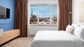 A hotel room with a large bed, a TV mounted on the wall, and a window with a cityscape view. - Siesta Boutique Smart Suites (Cluj-Napoca)