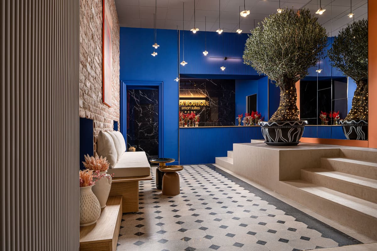 A modern hotel lobby with a blue accent wall, a marble fireplace, and a staircase leading to the upper floors.