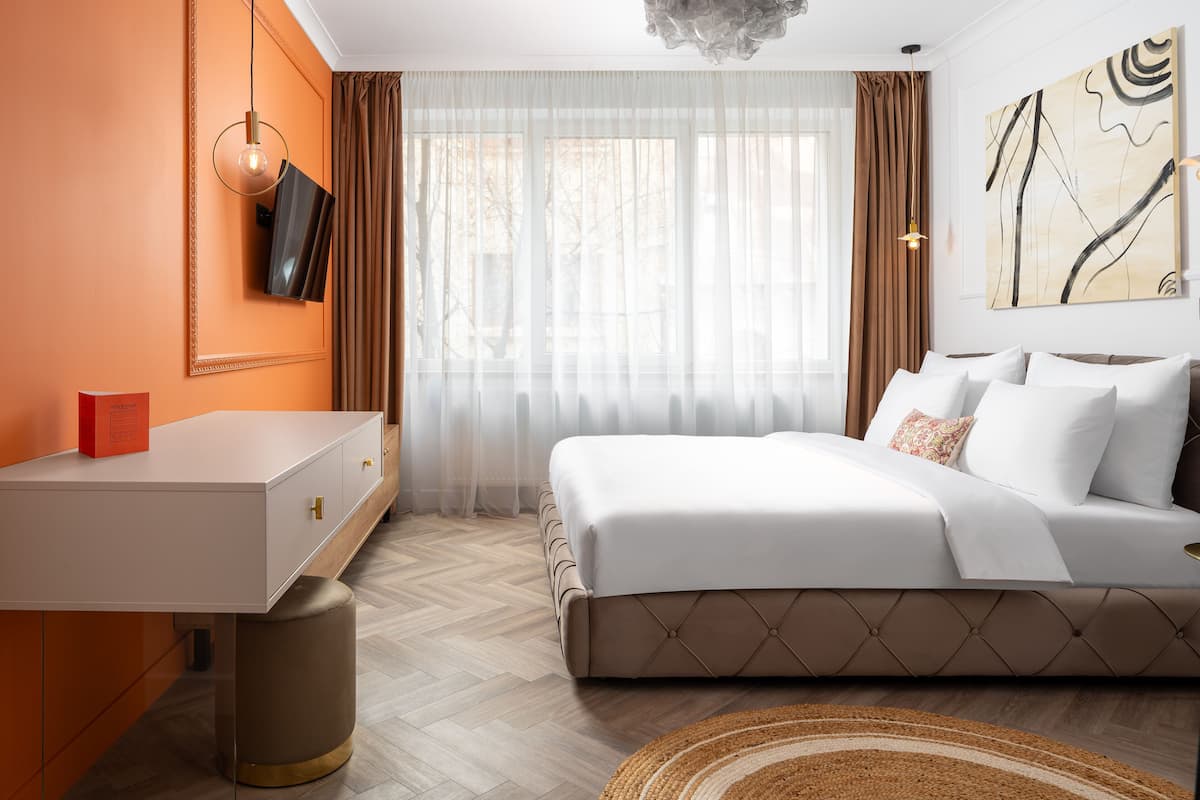 A bedroom with a bed, a desk, a chair, a TV, and a painting on the wall.