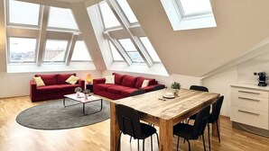Een modern loft appartement met een eethoek, twee rode banken, een salontafel en een keuken voorzien van een wit kastje en een koffieapparaat.