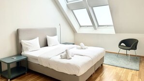 Een moderne slaapkamer met dakraam, een bed met witte lakens, een nachtkastje en een stoel.
