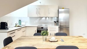 Een moderne keuken met witte kastjes, een roestvrijstalen koelkast, een houten eettafel met vier stoelen en een koffiezetapparaat op het aanrecht.