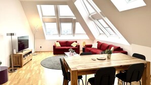 Een modern loft appartement met een eetgedeelte, een rode zithoek, een televisie en dakramen.