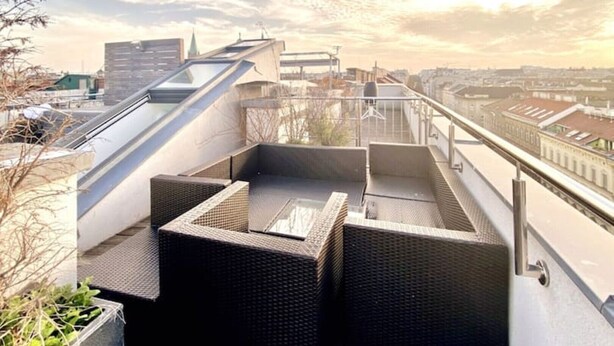 Een terras op het dak met een modern ontwerp, voorzien van een glazen omheining en een zitgedeelte buiten.