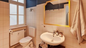 Un baño con inodoro, lavamanos, espejo y una toalla colgada en la pared.
