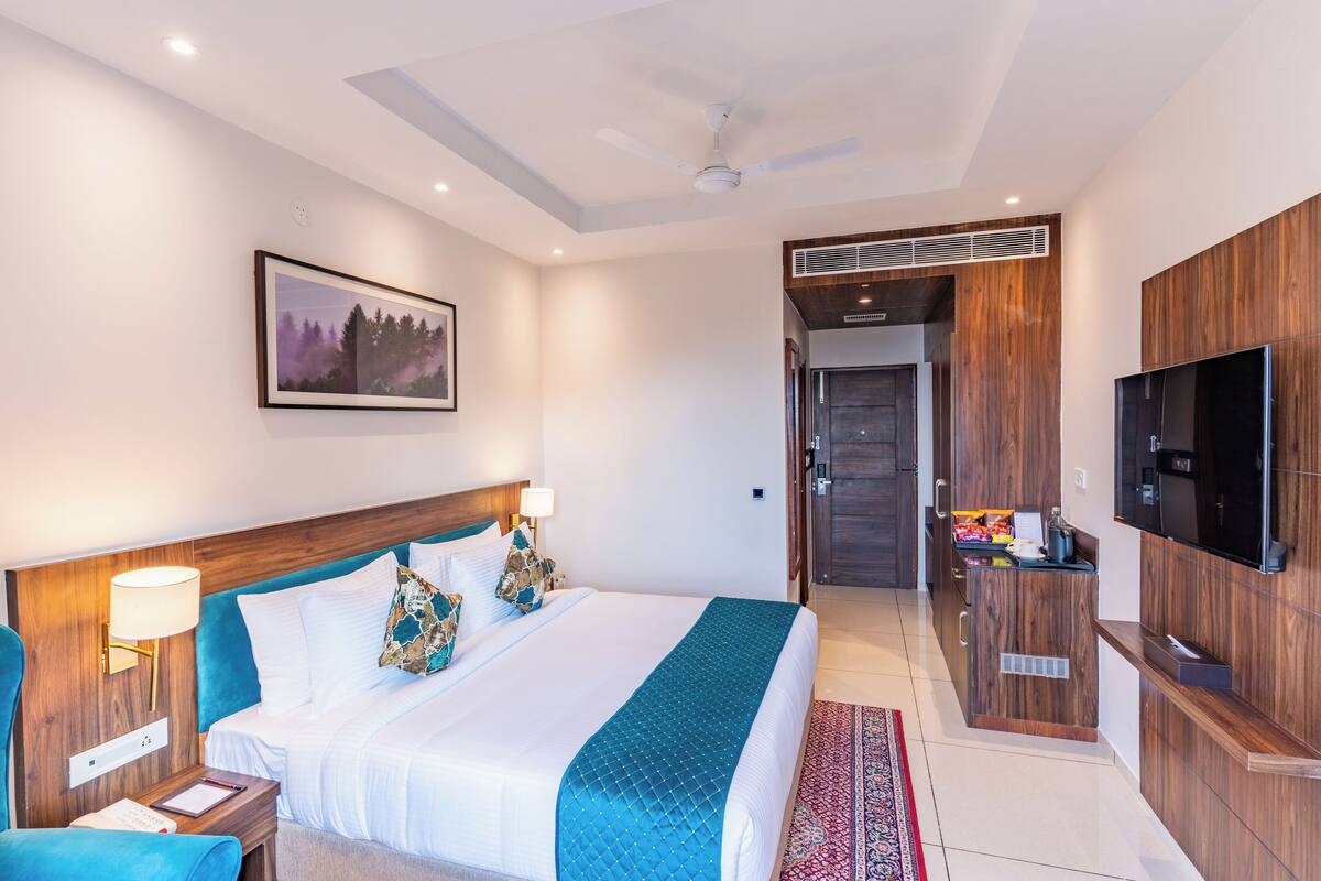 A modern hotel room with a large bed, a desk, a flat-screen TV, and a ceiling fan.