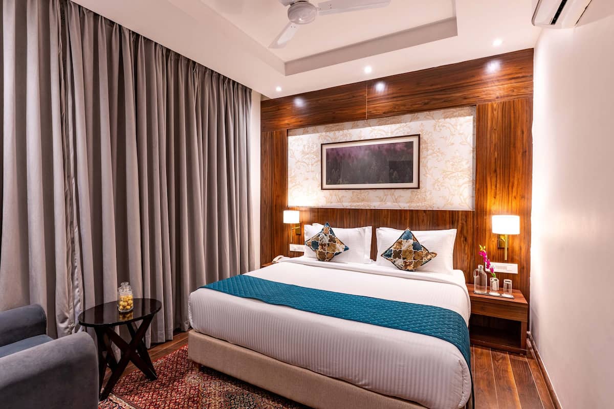 A hotel room with a large bed, a nightstand with two lamps, a small table with a vase, and a ceiling fan.