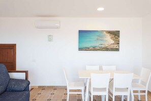 A dining area with a table and chairs, a painting of a beach, and a wooden door. - Villa Lucas - Magnificent Sea Views (San Jaime Mediterráneo)