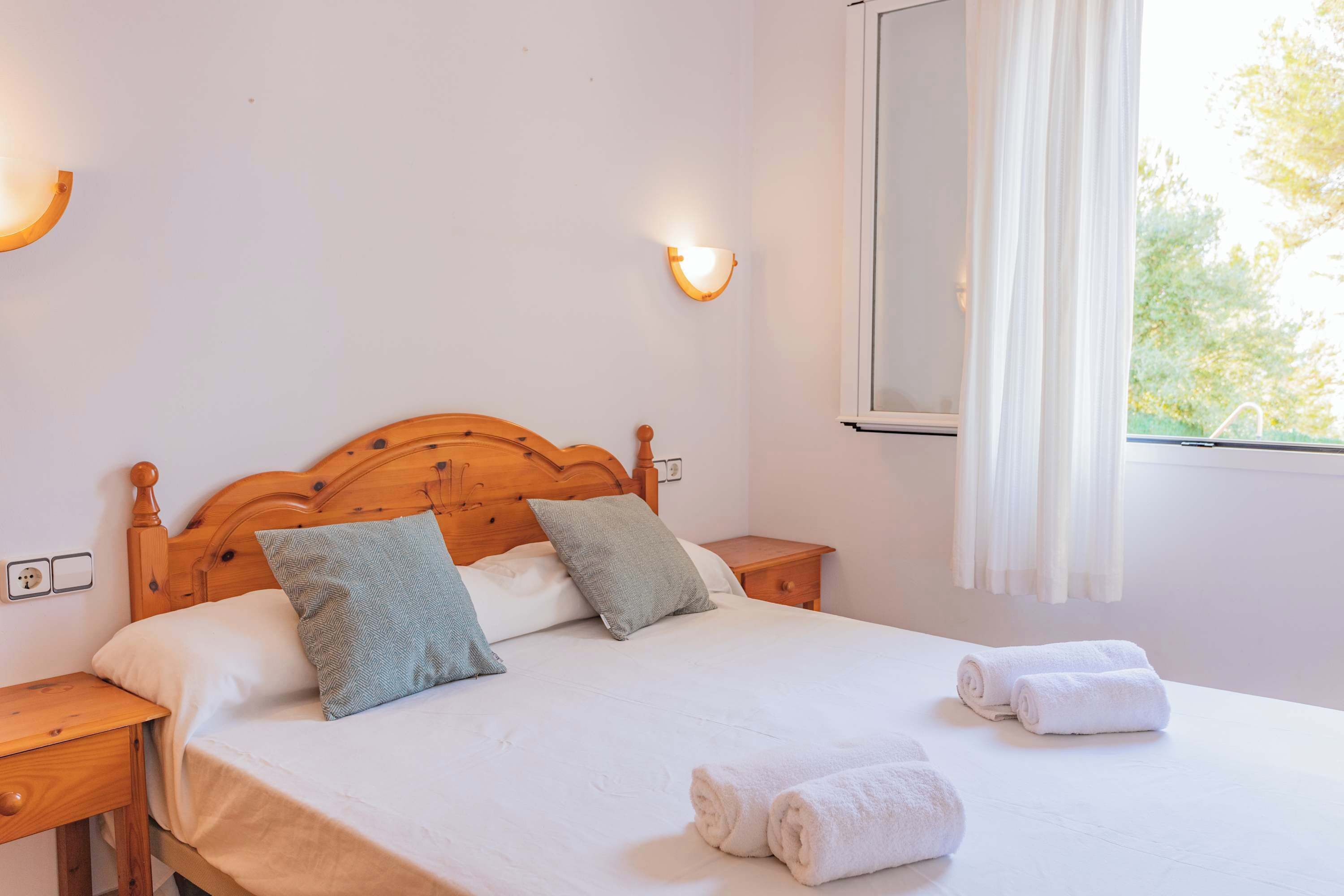 A neatly made bed with pillows, a wooden headboard, and two bedside tables with lamps.