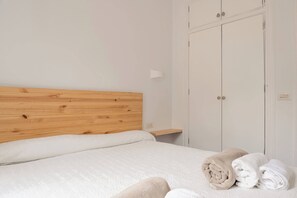 Une chambre à coucher avec une tête de lit en bois, un lit avec une literie blanche, une armoire et une petite table de chevet.
